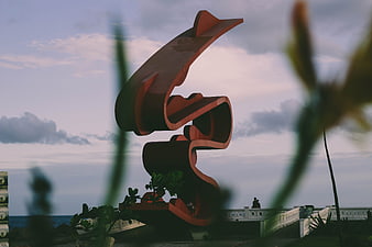 Red abstract sculpture against cloudy sky with blurred foreground