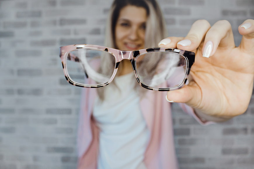 Woman holding tortoise shell glasses against brick wall