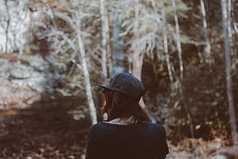 Woman in Baseball Cap Looking into Blurred Forest