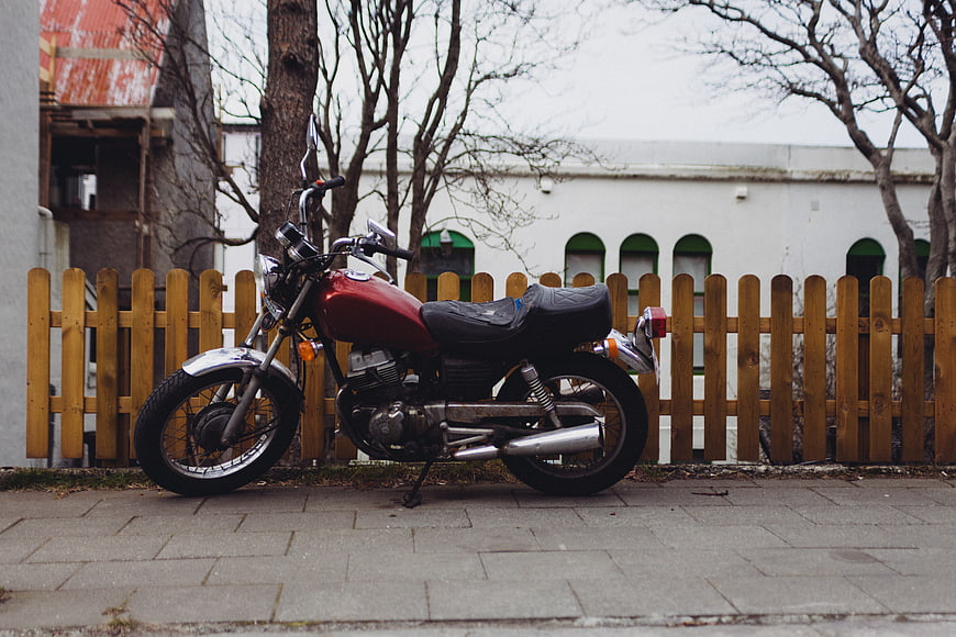 Vintage red motorcycle parked on sidewalk near wooden fence