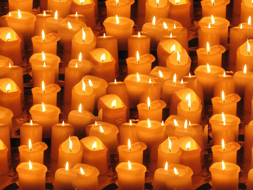 Close-up of many lit yellow candles with warm glowing flames