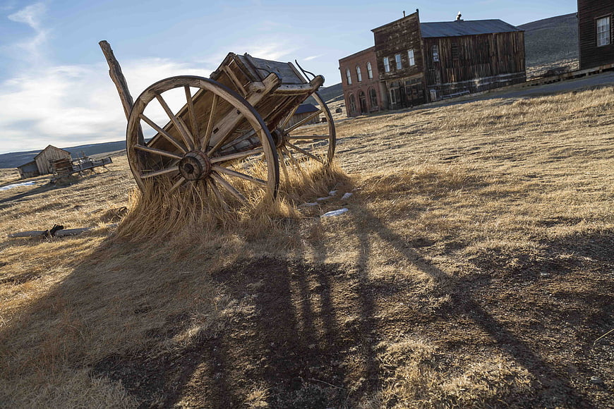 Abandoned wooden wagon in dry grass near old western buildings