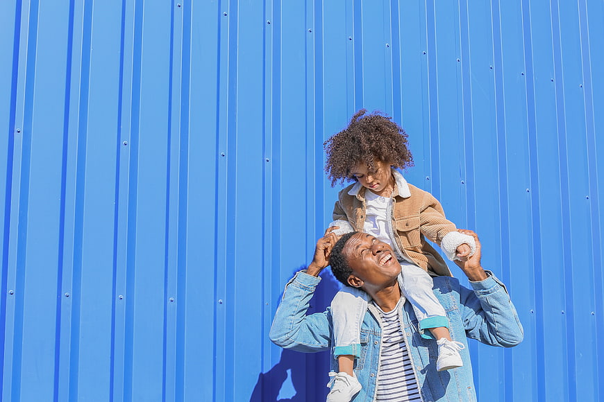 Happy Father Carrying Daughter on Shoulders Against Blue Wall