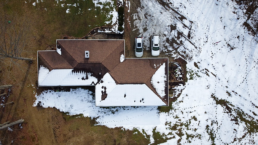 Aerial view of suburban house with snow-covered roof and cars