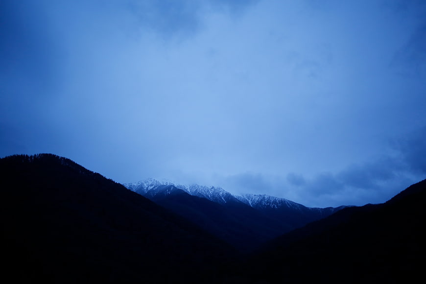 Dark Blue Mountain Landscape with Snowy Peaks and Clouds