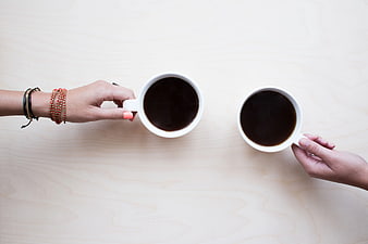 Top View of Two Hands Holding Coffee Mugs on Wooden Table