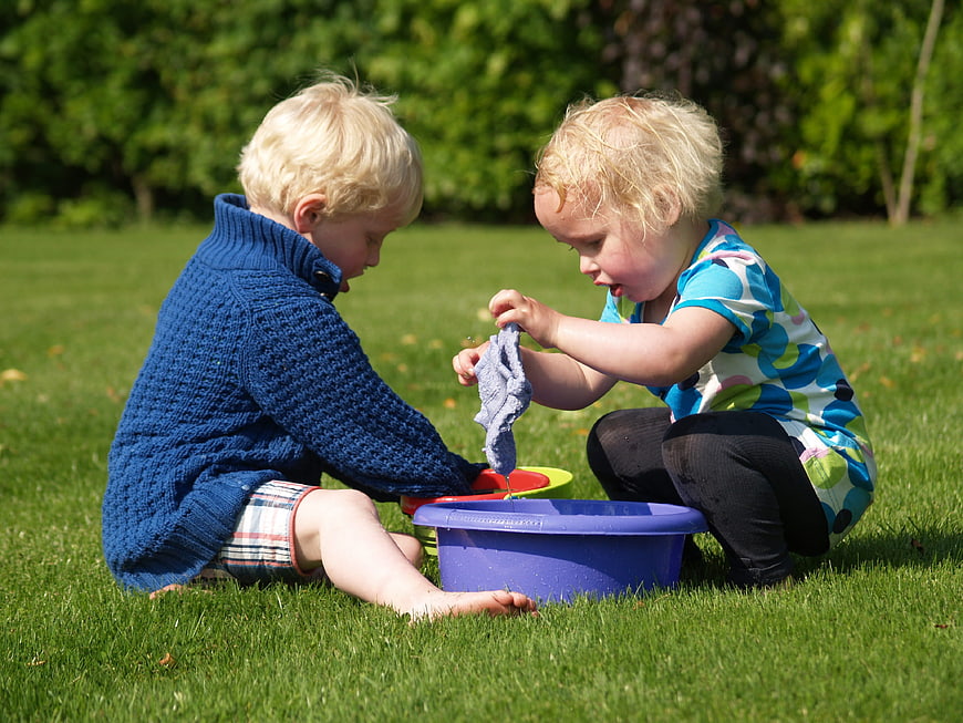 Two toddlers playing with water and washcloth on grass