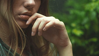 Close-up portrait of a woman with hand near lips in nature