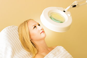 Woman Receiving Facial Treatment With Magnifying Lamp