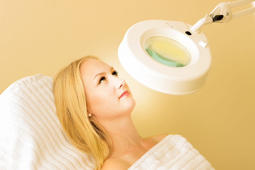Woman Receiving Facial Treatment With Magnifying Lamp