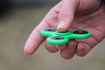 Hand holding green fidget spinner toy close up