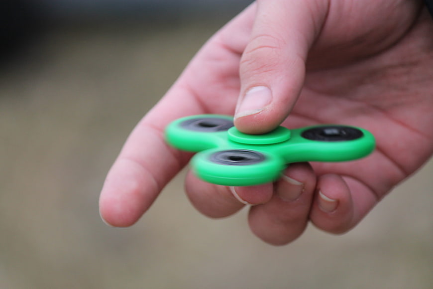 Hand holding green fidget spinner toy close up