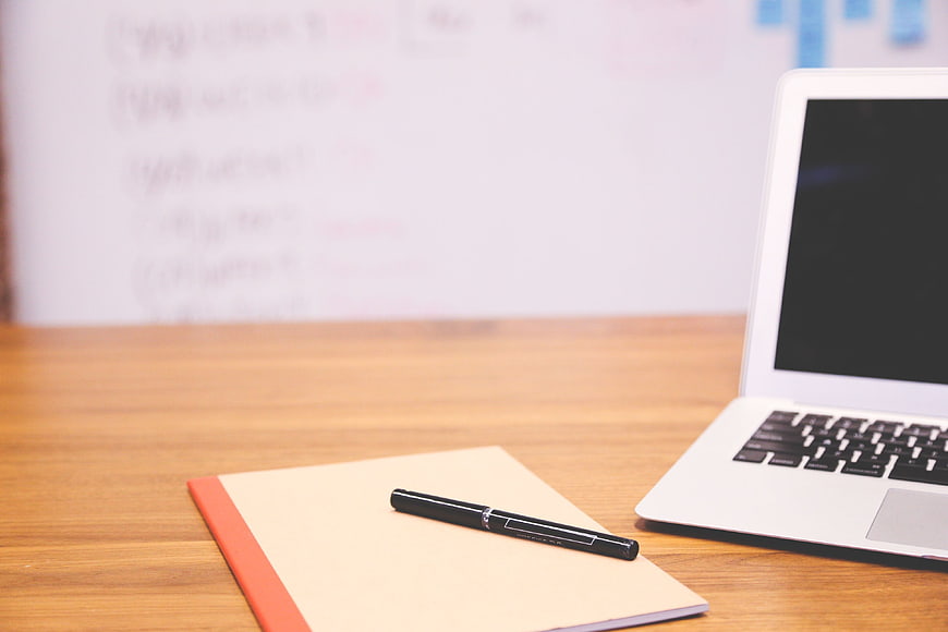 Laptop and Notebook on Wooden Desk with Whiteboard Background