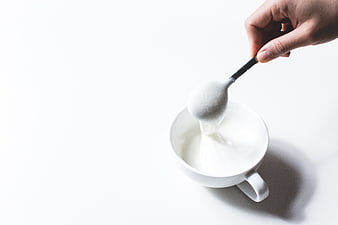 Hand Scooping White Cream into Cup on White Background