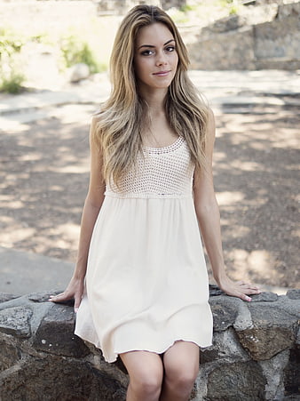 Young Woman in White Dress Sitting on Stone Wall Outdoors
