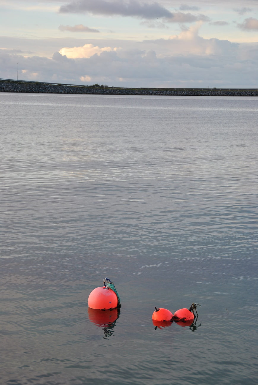 Orange buoys floating in calm sea water with distant breakwater
