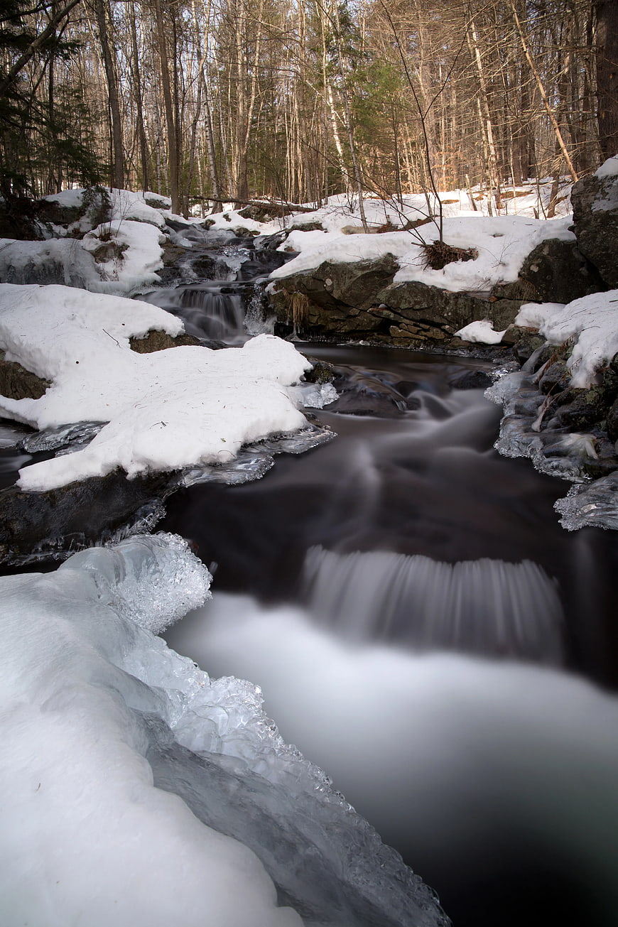 Long Exposure Winter Stream Flowing Through Snowy Forest