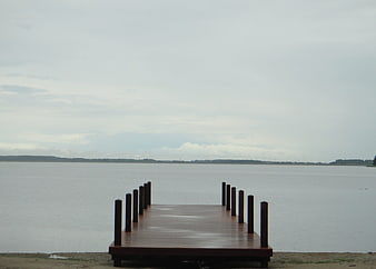 Empty wooden pier extending into calm lake under overcast sky