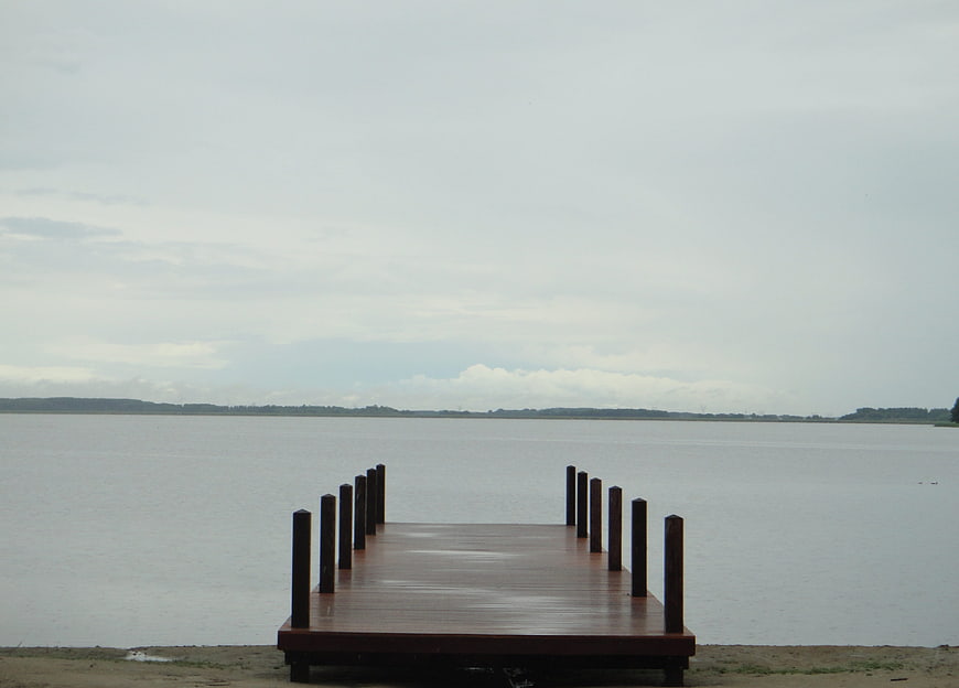 Empty wooden pier extending into calm lake under overcast sky