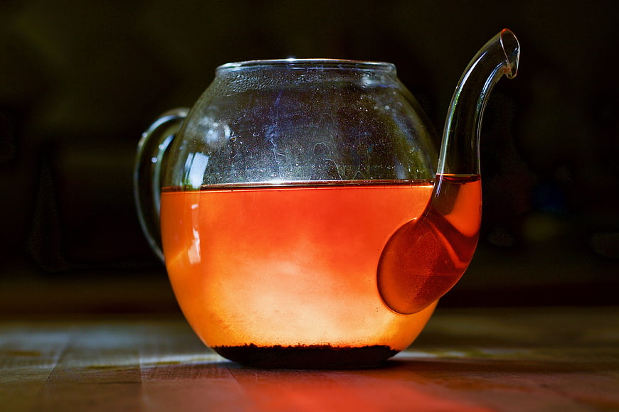 Glass teapot with glowing amber tea on wooden table