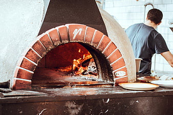 Wood-fired brick pizza oven with burning logs in kitchen