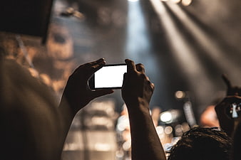 Hands holding smartphone recording concert stage