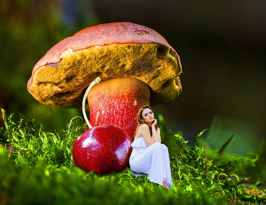 Tiny woman sitting next to giant mushroom and cherry in forest