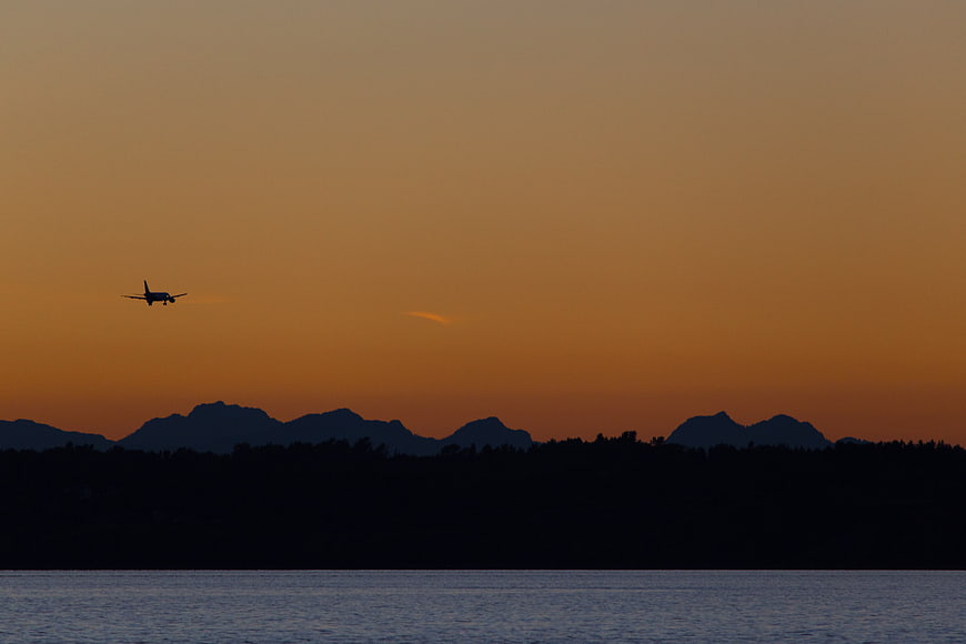 Silhouette of Airplane Landing Over Lake at Sunset