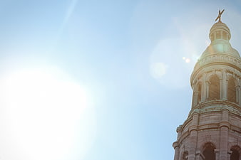 Sunlit church tower with cross against blue sky