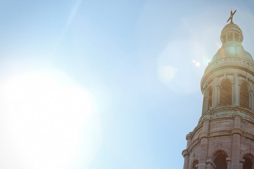 Sunlit church tower with cross against blue sky