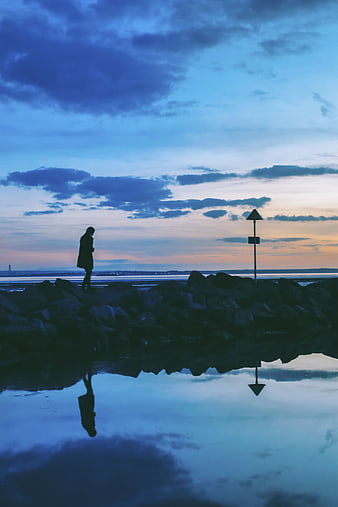 Silhouette of person walking on rocks at twilight with reflection