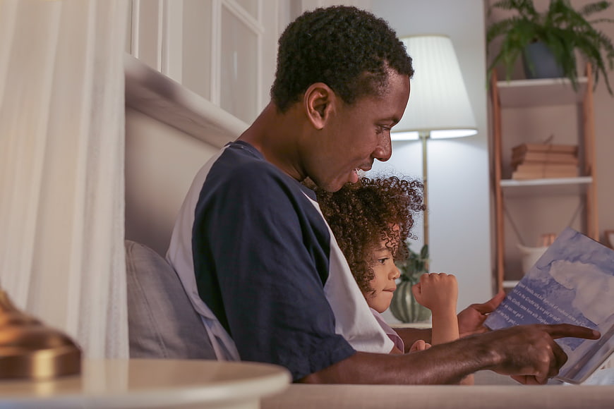Father reading bedtime story to young daughter on bed