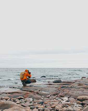 Photographer in Orange Jacket Taking Photos on Rocky Coast