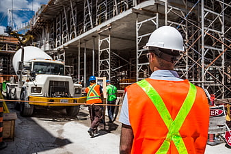 Construction worker in safety vest observing site with concrete truck