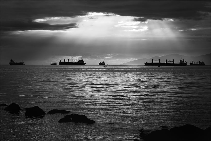 Silhouetted Cargo Ships on Ocean with Dramatic Sunbeams