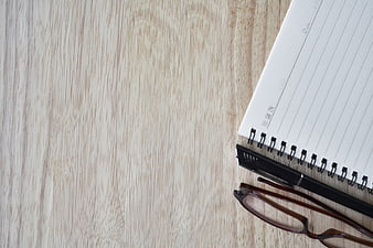 Flat lay of notebook, pen, and glasses on light wood table