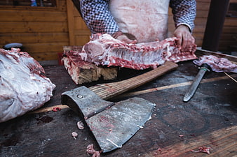 Butcher cutting pork ribs with axe on wooden table