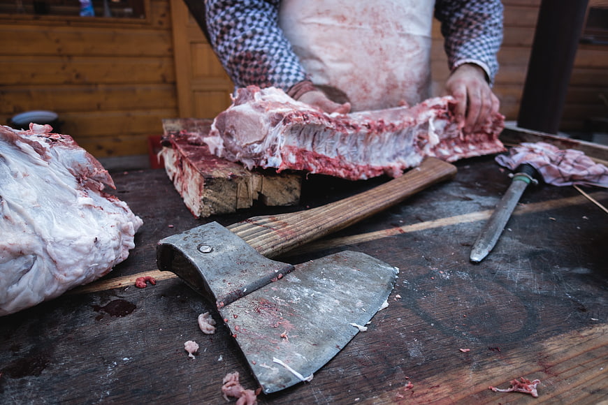 Butcher cutting pork ribs with axe on wooden table