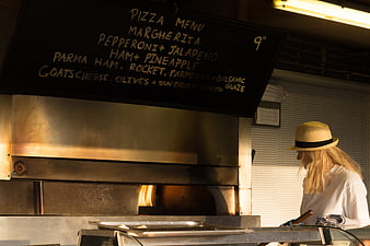 Woman in straw hat cooking pizza in wood-fired oven