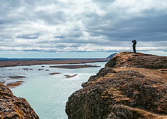 Lone traveler standing on rocky cliff overlooking glacial river