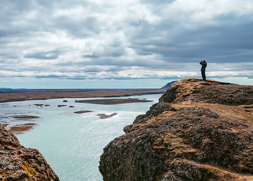 Lone traveler standing on rocky cliff overlooking glacial river