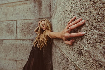 Blonde woman leaning against textured stone wall