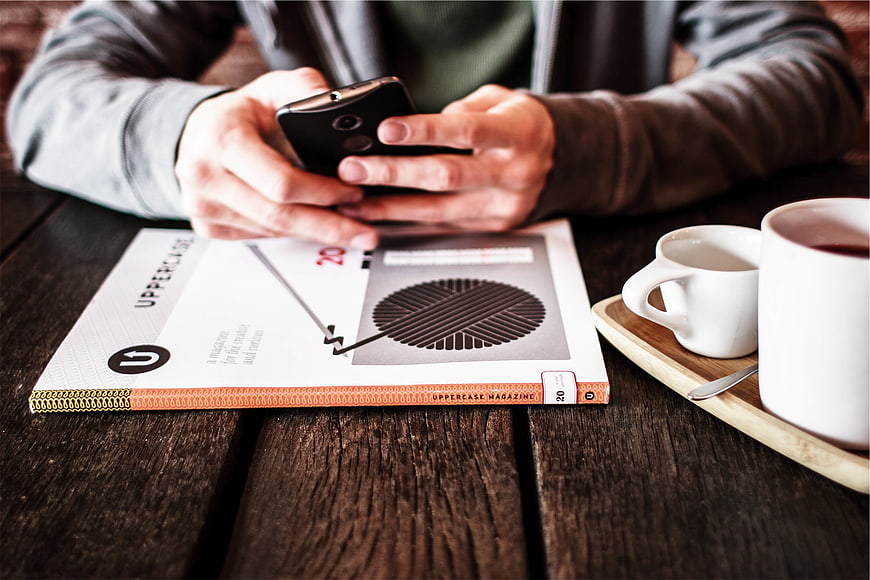 Person using smartphone with magazine and coffee on wooden table