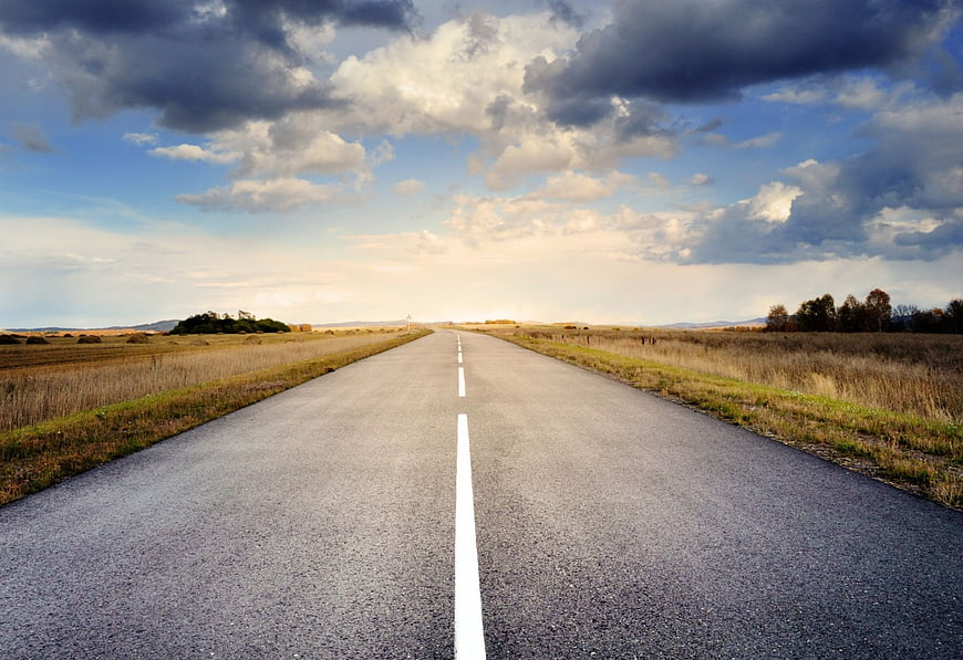 Straight asphalt road stretching to horizon under dramatic cloudy sky