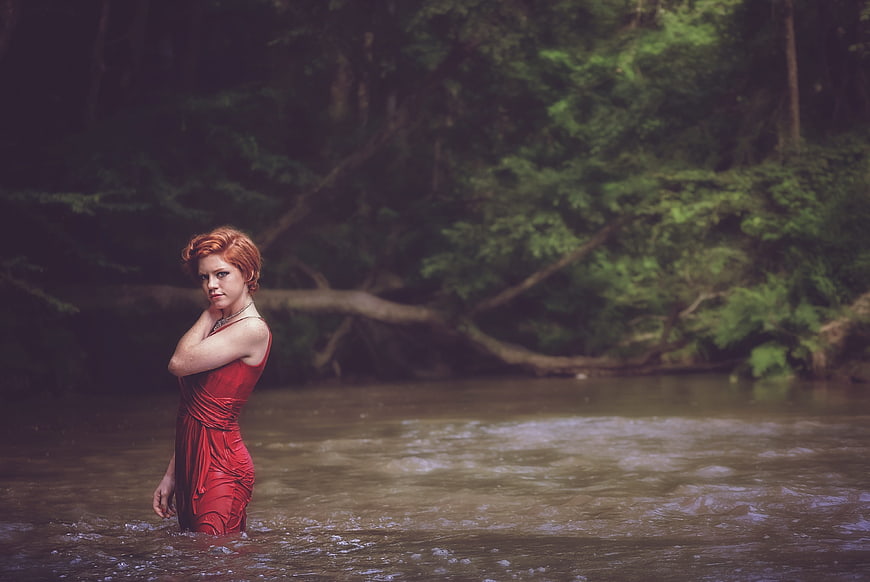 Redhead woman in red dress standing in river