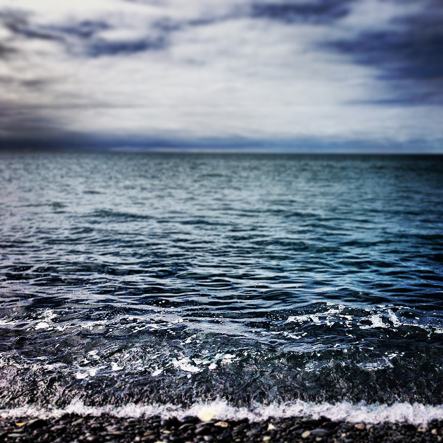 Dramatic Ocean Waves on Pebble Beach Under Cloudy Sky