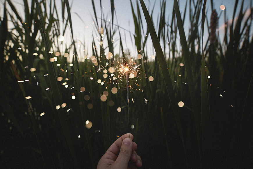 Hand holding sparkler in tall grass at dusk