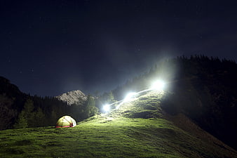 Camping tent on grassy mountain ridge under starry night sky