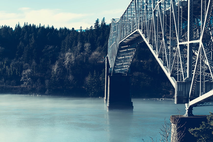 Steel truss bridge over misty river with forest background