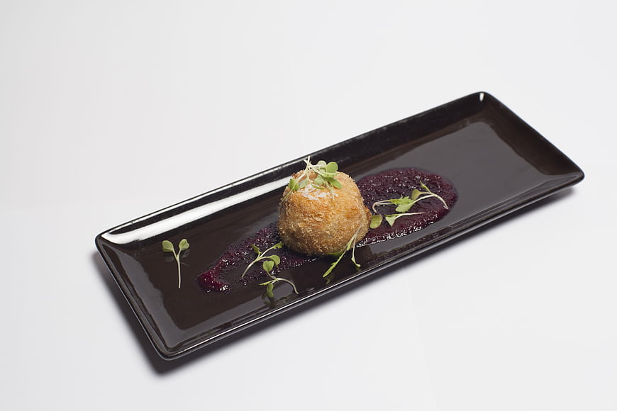 Gourmet fried appetizer with berry sauce on black rectangular plate